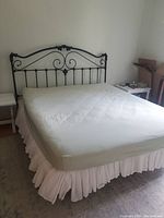Full view of California King bed assembled with green fitted sheet, white bed skirt, and gray wrought iron headboard with scroll details.