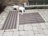 Two mats laid out on stone outdoor flooring with two white step stools.