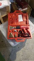 Open red plastic carrying case showing Milwaukee heat gun with attached cord and four nozzle attachments