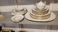 Full set arranged on shelf showing stacked plates, small bowls, and lidded sugar bowl with gold trim.