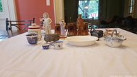 Wide view of lot showing diverse items including ceramic figurines, blue and white porcelain, amber glassware and wooden figure on table.