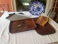 Overview of all platters and baking sheets on a table, including blue and white platter on a stand, Pampered Chef stoneware, wooden platters, and metal baking sheets.