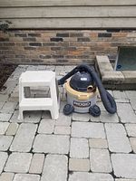 Rigid shop vac and Rubbermaid step stool shown on paved surface outdoors.