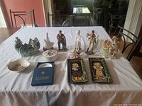 Photo showing the full collection including various porcelain figurines, decorative trays, and containers arranged on a white cloth on a table.