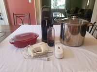 Photo showing all items together on a table: SodaStream machine, carbonating bottle, red cherry pitter, hand beater with switch, large stock pot with lid.