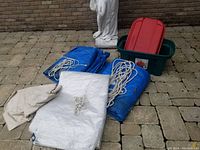 Photo showing two blue tarps, one white tarp and one beige canvas piece with eyelets, along with several coiled white ropes.