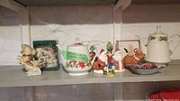 Shelf with assorted Christmas-themed teapots, figurines, pitcher, and ornaments showing the grouping of items in the lot