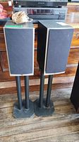 Pair of Athena Technologies speakers on metal stands with fabric grilles on front