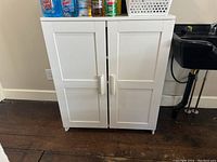Full view of white laminate cabinet, showing two front doors, standing on a wooden floor next to a utility sink.
