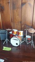 Miniature Yamaha drum set with various drums and cymbals on stands, placed on a wooden surface.