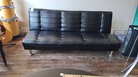 Front view of the black faux leather futon couch showing horizontal tufted upholstery and metal legs.