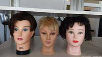Three rubber head mannequins displayed together, showing hair styles and facial features.