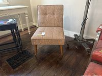 Single mid-century modern style upholstered chair with patterned beige fabric and wooden legs shown from front angle.