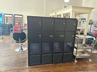 Front view of black laminate shelf unit with 16 cubbies arranged in 4x4 grid with doors, plastic and fabric bins