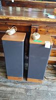 Pair of Advent Prodigy Tower speakers standing side by side on wooden floor with speaker wires coiled on top.