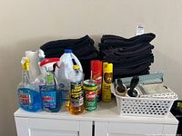 Photo showing black hand towels stacked behind assorted cleaning bottles including Sparkle & Shine, Windex, Mr. Clean Pine Cleaner, and Comet cleanser.