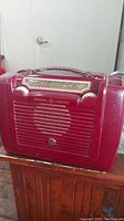 Front view of the burgundy General Electric vintage radio showing the speaker grille, tuning dial, and carrying handle.