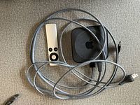 Photo showing Apple TV third generation device, silver remote control, and power and HDMI cables.