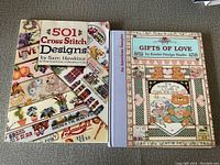 Two cross stitch books, 501 Cross Stitch Designs and Gifts of Love, showing front covers with various colorful stitch patterns and motifs.