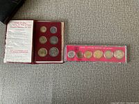 Photo showing 1970 Bank of Israel Specimen Set in maroon holder alongside 1971 Official Mint Set in red casing