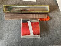 Photo of unopened folding fan inside a decorative Cathay Pacific-branded box, along with a red fabric pouch with floral design.