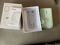 Photo showing the label maker device, user manual, USB cable, and original box.