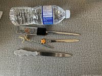 Four letter openers of various designs placed next to a water bottle for size comparison.