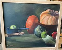 Full front view of the oil painting showing the still life scene featuring pumpkins, apples, a bowl, and a cast iron pot on a dark surface. The canvas is framed in a light wood frame.