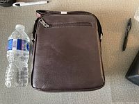 Front view of the brown leather crossbody bag showing zippered compartment and texture.