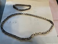Two sterling silver chain pieces on paper showing handwritten weights and 0.925 marking, smaller piece is bracelet, larger is necklace
