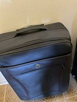 Full view of the black soft shell Heys suitcase with red stitching and top handle.