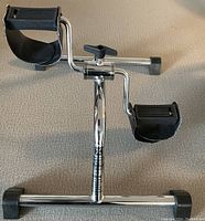 Full view of the tabletop pedal exercise bike, showing chrome frame, adjustable foot pedals with straps, and rubber feet for stability.