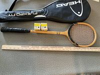 Two wooden tennis racquets laid out side by side with a black HEAD racquet cover, a wooden ruler for scale, and two small yellow and white boxes of Dunlop tennis balls on top.