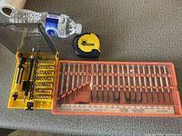 Photo showing the precision screwdriver bit set in yellow case, yellow and black tape measure, and a set ruler with measurements underneath them.