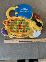 Yellow VTech Buzz the Spelling Bee educational toy with alphabet buttons and a blue flip-open book on bee body and ruler for size reference.