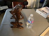 Full view of the dark wood carved figurine seated cross-legged with the object in hand, with a water bottle for scale.