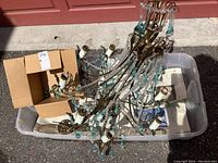 Overhead view of the chandelier in a plastic bin showing brass arms and turquoise glass drops alongside a box.