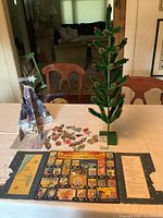 Photo showing green bottle brush Christmas tree decorated with red pom-pom berries, Story of Christmas advent calendar laid flat, and various cardboard cutouts arranged in front.