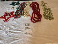 Full view of six Christmas garlands laid out on a white tablecloth, showing variety of colors and styles including stars, beads, and gold leaves.
