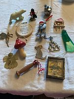 Photo shows fourteen assortment of Christmas ornaments including miniature Alessi kettle by Alessi, polar bear, bear with ski poles, squirrel, mushroom, green sled, and various metal and wood ornaments.
