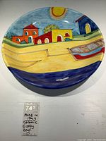 Front view of large ceramic display bowl with colorful Mediterranean seaside scene, showing vibrant houses, boat, and sun design.