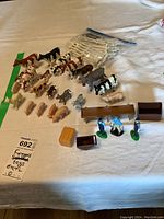Top down photo of all 23 farm animal toys and accessories displayed on a table with a label stating 'Farmyard toys Ertl'. Items include multiple farm animals, white fence pieces, feeding troughs, a hay bale, and three human figurines.