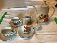 Full view of children's china coffee set including coffee pot, creamer, sugar bowl, cups, and saucers on fabric background
