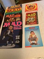 Seven Mad Magazine paperback books spread out on a table showing varied themes from different decades.