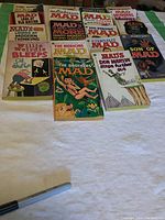 Photo showing 13 Mad Magazine vintage paperback books laid out on a cloth, titles visible on covers, condition visibly worn.