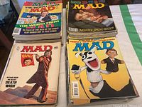 Stack of Mad Magazines showing various colorful covers with caricatures and typical Mad Magazine humor style from the 70s-90s, worn condition.