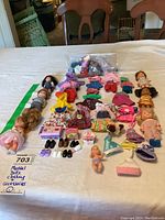 Photo showing six Mattel mini dolls and a large variety of assorted doll clothing and accessories laid out on a table.