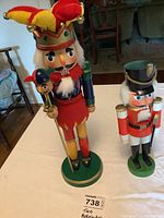 Two wooden nutcrackers, one with jester hat holding scepter and one traditional soldier nutcracker on white table