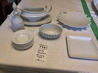 Overview of six white porcelain serving ware pieces arranged on a table including cruet, sauce dishes, gravy boat with tray, leaf-shaped and square dishes.