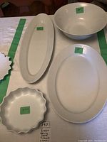 Four white porcelain serving pieces displayed on a table: 9-inch fluted dish, 13-inch bowl, 18-inch oval platter, and 23-inch long oval dish.